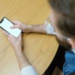 Pessoa segura um smartphone com a tela em branco sobre uma mesa de madeira.