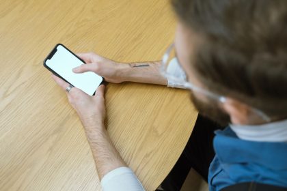 Pessoa segura um smartphone com a tela em branco sobre uma mesa de madeira.