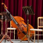Palco vazio preparado para um concerto, com um violoncelo e estantes de partituras.