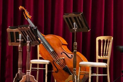 Palco vazio preparado para um concerto, com um violoncelo e estantes de partituras.
