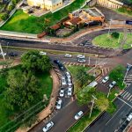 Vista aérea de um cruzamento urbano movimentado, com veículos circulando por diferentes vias.