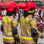 Dois bombeiros usando capacetes vermelhos participam de um evento público de segurança ao ar livre.