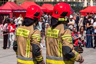 Dois bombeiros usando capacetes vermelhos participam de um evento público de segurança ao ar livre.