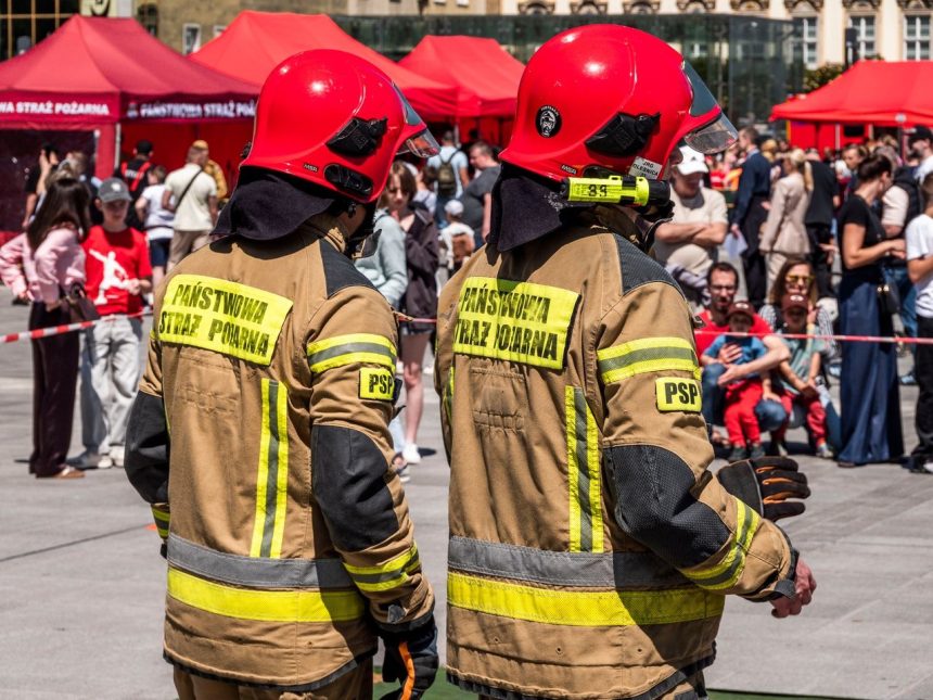 Dois bombeiros usando capacetes vermelhos participam de um evento público de segurança ao ar livre.