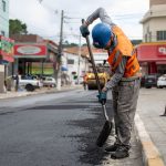 Trabalhador pavimenta uma rua com uma pá durante uma obra viária.