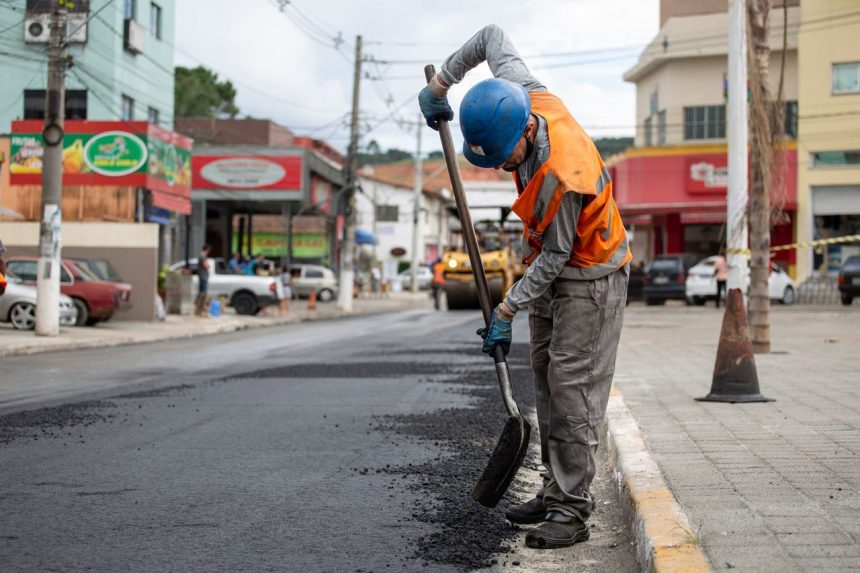 Trabalhador pavimenta uma rua com uma pá durante uma obra viária.