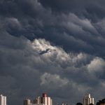 Nuvens escuras e carregadas se aproximam de edifícios em uma área urbana.