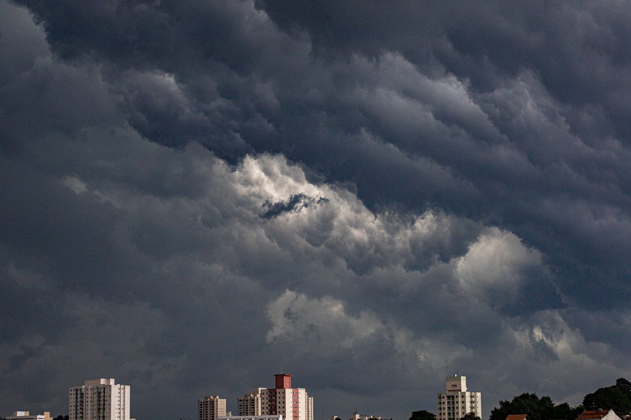 Nuvens escuras e carregadas se aproximam de edifícios em uma área urbana.