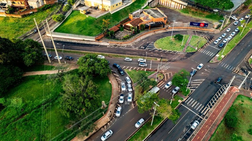 Vista aérea de um cruzamento urbano movimentado, com veículos circulando por diferentes vias.